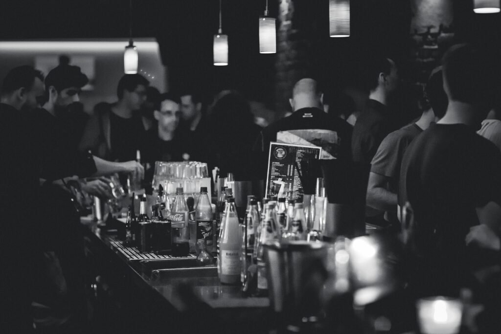pexels-photo-274192-274192 Black and white photo capturing the lively atmosphere in a bar with people socializing and a busy bartender serving drinks.